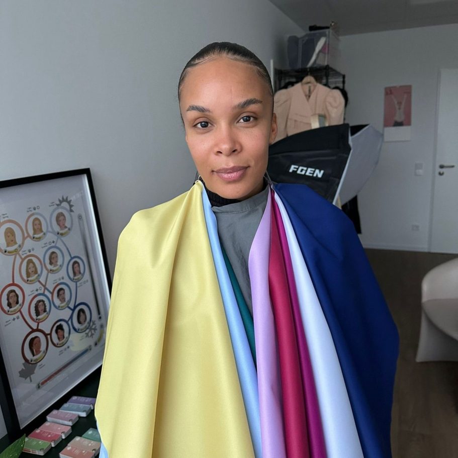 Frau mit bunten Stoffen um den Oberkörper, im Hintergrund ein Arbeitsplatz.